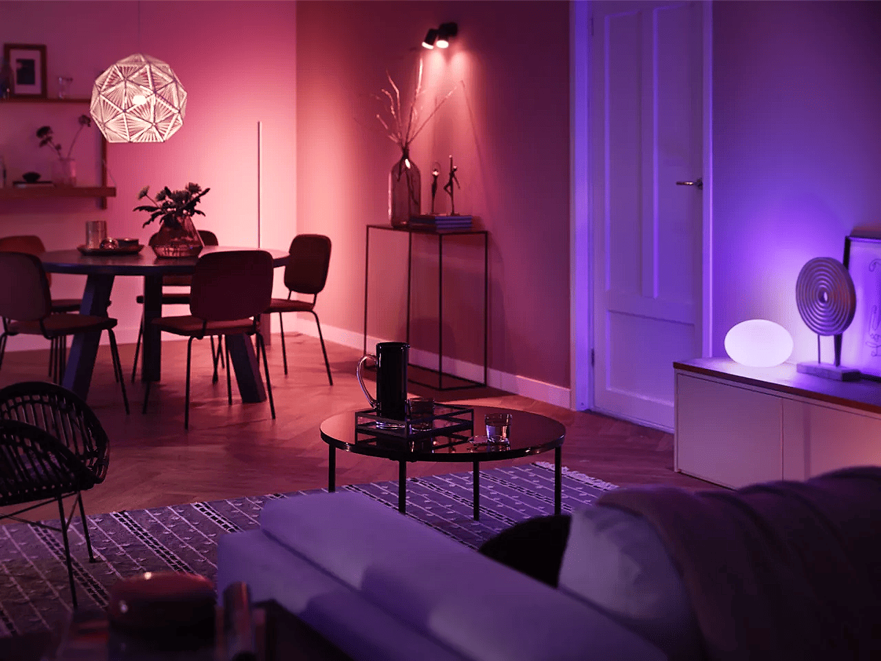 Moderne stue og spisestue opplyst med Philips Hue smartbelysning i ulike farger som rosa, lilla og varmt spotlys, som skaper en stemningsfull atmosfære.